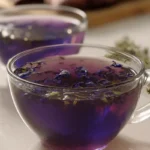 A clear cup of Brazilian Mounjaro recipe tea, steeped with dried butterfly pea flowers, showcasing its deep purple hue on a light countertop.