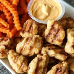 Grilled chicken nuggets served with crinkle-cut sweet potato fries and dipping sauce on a white plate, Chick fil a grilled nuggets recipe copycat.