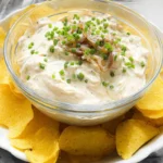 Creamy Lipton onion dip recipe served in a glass bowl, topped with caramelized onions and chives, surrounded by golden potato chips.