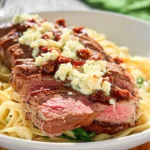 Plated steak gorgonzola recipe featuring sliced steak, crumbled Gorgonzola cheese, and sun-dried tomatoes over creamy fettuccine pasta.