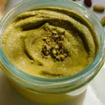 Smooth homemade pistachio butter in a glass jar, topped with crushed pistachios for garnish.