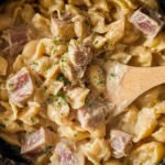 Close-up of creamy tuna helper recipe in a skillet with tender pasta shells and chunky tuna, topped with black pepper and parsley.