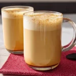 Two glass mugs filled with a frothy eggnog latte on a red napkin – festive and creamy eggnog latte recipe served hot.