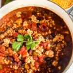 A hearty bowl of healthy ground chicken chili recipe, filled with black beans, kidney beans, tomatoes, and bell peppers, garnished with fresh cilantro.