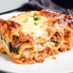 Close-up of a cheesy slice of Healthy Ground Chicken Lasagna, layered with tender noodles, rich meat sauce, and melted mozzarella on a white plate.