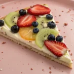 A photo of a delicious-looking dessert with a variety of fruits as toppings, including strawberries, blueberries, and a slice of citrus fruit. The toppings are artistically arranged on a shallow, rounded dish with a soft, muted pink hue. The toppings create a visually appealing contrast with the creamy base of the dessert. The image is a close-up, high-resolution photograph that emphasizes the textures and colors of the toppings and the dish itself. The toppings are fresh and vibrant, with the blueberries providing a deep, rich color, and the strawberries adding a bright, juicy element.