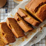 A freshly baked loaf of pumpkin bread sliced on a wire rack, showing its soft and moist texture with golden-brown crust.