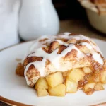 Close-up of Apple Pie Biscuits with cinnamon-spiced apple filling and vanilla glaze on a white plate.