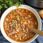Close-up of homemade 15 bean soup filled with mixed beans, vegetables, and herbs, served with crusty bread.