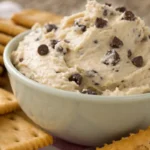A bowl of creamy cookie dough dip filled with chocolate chips served with crackers for dipping