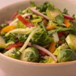 A fresh brussel sprout salad made with shaved sprouts greens and vegetables served in a bowl.