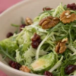 A fresh brussel sprout salad made with shaved sprouts greens and vegetables served in a bowl.