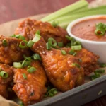 Crispy buffalo chicken wings coated in spicy sauce and served on a platter with celery sticks and dipping sauce.