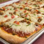 A large sheet pan pizza with thick crust, melted cheese, and assorted toppings fresh from the oven.