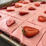 Strawberry sheet cake topped with pink frosting and fresh strawberry slices baked in a large pan and cut into neat squares.