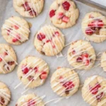 Strawberry shortcake cookies with pink crumb topping and creamy centers arranged on a plate, decorated with fresh berries for a cute bakery style dessert display.