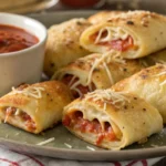 Golden baked homemade pizza rolls filled with melted cheese and sauce, made from soft pizza dough and served warm with a side of dipping sauce.