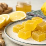 Honey lemon turmeric gummies shaped in small molds, with a golden color, arranged on a plate with lemon slices and fresh ginger, highlighting a soft chewy texture and natural ingredients.