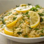 Lemon orzo served in a bowl with fresh herbs and a light citrus sauce, styled as a Mediterranean orzo side dish or lemon chicken orzo pasta option