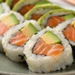 Salmon avocado roll sliced into bite sized sushi pieces with fresh salmon, avocado, and rice wrapped in seaweed, served on a plate as a classic homemade sushi roll.