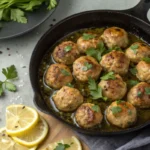Overhead view of golden turkey meatballs in a cast iron skillet with glossy lemon herb pan sauce, garnished with fresh parsley and lemon slices — easy one skillet turkey meatballs with lemon herb sauce for a healthy weeknight dinner.