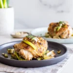 Garlic & Onion Roasted Chicken Thighs with Leeks served on a white plate with caramelized vegetables