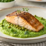 Pan-Seared Salmon with Pea Purée plated on white dish with crispy golden skin and vibrant green purée