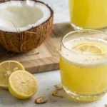 Lemon Turmeric Coconut Water Drink in a tall glass with ice and lemon wheel garnish on a white marble surface