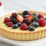Lemon tart with mixed berries on a white plate showing golden crust and colorful berry topping