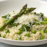 Spring Vegetable Risotto with Parmesan served in a white bowl with fresh asparagus, peas, and zucchini visible throughout the creamy rice
