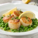 Lemon butter scallops with spring peas plated on white dish with golden seared crust and fresh herbs