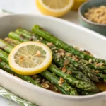 Asparagus with Lemon Brown Butter served on a white platter with fresh parsley and shaved Parmesan cheese