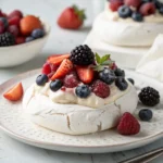 Mini Pavlova with Fresh Berries served on white plates with whipped cream and colorful mixed berries on top