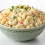 Creamy macaroni salad in a white serving bowl with colorful vegetables and fresh herbs