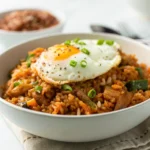 Crispy kimchi fried rice in a white bowl topped with a fried egg and green onions