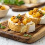 Mango chutney and brie crostini arranged on a white serving platter with fresh basil garnish