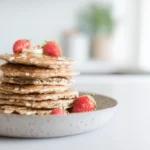 Banana Oat Blender Pancakes stacked on a white plate with maple syrup drizzle and fresh banana slices