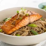 Miso glazed salmon with soba noodles served in a white bowl with sesame seeds and scallions