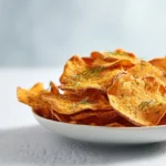 Oven-baked sweet potato chips arranged on a white plate with golden crispy edges and sea salt