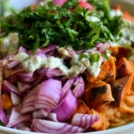 Sweet potato bowl with roasted cubes, grilled chicken, avocado, greens, and tahini dressing on a white plate
