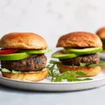 Grilled turkey burgers with avocado on toasted buns with fresh lettuce and tomato on a white plate