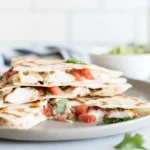 Grilled Chicken and Cheese Quesadillas cut into triangles on a white plate with salsa and sour cream
