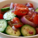 Cucumber tomato onion salad in a white bowl with fresh vegetables and vinaigrette dressing