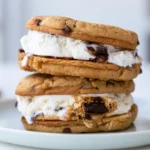 Ice cream sandwich dessert layered with whipped cream and chocolate sauce on white plate