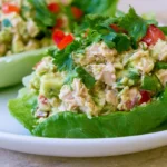 Tuna Avocado Salad in Lettuce Cups arranged on white plate with fresh herbs and lemon wedges