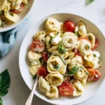 Tortellini Caprese Pasta Salad in white bowl with fresh mozzarella, cherry tomatoes, and basil leaves drizzled with balsamic glaze