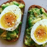 Avocado toast on sourdough bread topped with cherry tomatoes and microgreens on a white plate