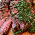 Chimichurri flank steak sliced and arranged on a white platter with fresh herb sauce drizzled over the top