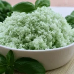 Basil salt recipe in a glass jar with fresh basil leaves scattered on a white marble counter