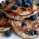 Blueberry Cottage Cheese Pancakes stacked on a white plate with fresh blueberries and maple syrup